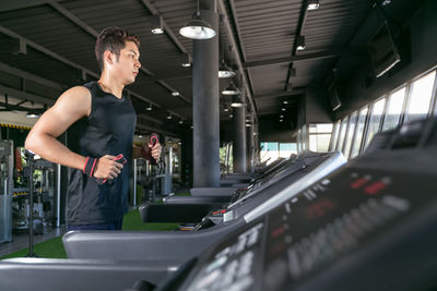 Side view of young man exercising on treadmill in gym