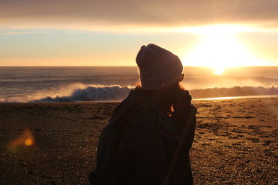 Rear view of woman looking at sea against sky during sunset