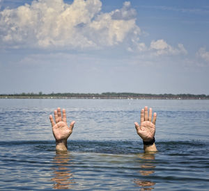 Cropped hands drowning in lake against sky