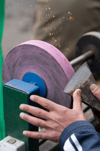 Master sharpens ax on electric sharpener with bright sparks and holds blade with his brutish fingers