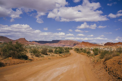 Dirt road passing through landscape against cloudy sky