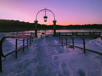 Snow covered railing against sky during sunset