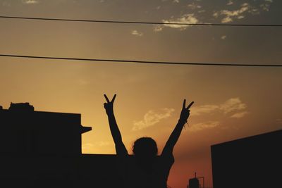 Silhouette people with arms raised against sky during sunset