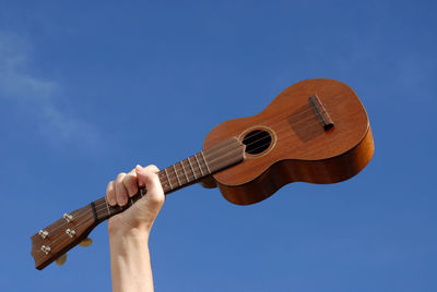 Low angle view of hand playing guitar against blue sky