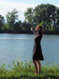 Woman standing by lake against trees