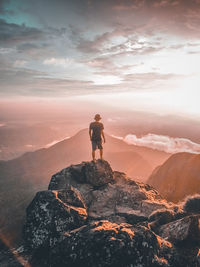 Man standing on rock by mountain against sky