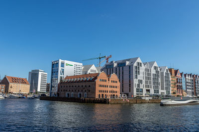 Buildings by river against clear blue sky