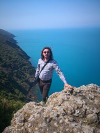 Portrait of man standing on rock against sky