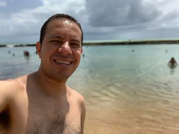 Portrait of shirtless man at beach against sky