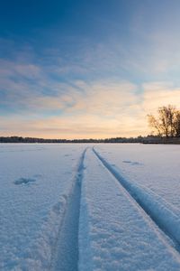 Tire track on snowy landscape against sky during sunset