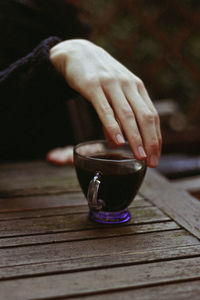 Cropped hand of woman with coffee on wooden table in cafe