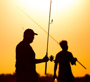 Silhouette man fishing against orange sky