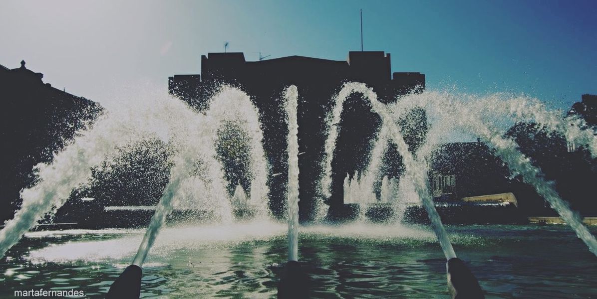 water, fountain, building exterior, built structure, waterfront, architecture, reflection, clear sky, motion, splashing, sky, nature, sunlight, spraying, tree, outdoors, sunbeam, sea, day, beauty in nature