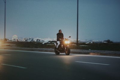 Man riding motorcycle on road against sky in city