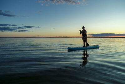 Rear view of man jumping in sea against sky during sunset