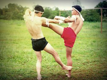 Shirtless male fighters practicing on grass against sky