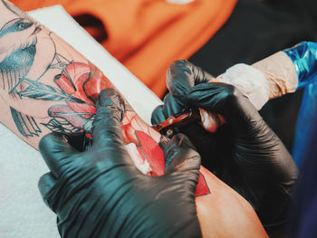 Cropped image of female artist making tattoo on male customer hand