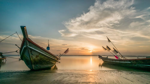 Sailboats moored on sea against sky during sunset