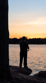 Rear view of silhouette man standing at beach against sky during sunset