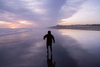 Rear view of woman standing at beach against sky during sunset