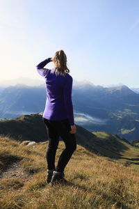 Rear view of woman sitting on mountain against sky