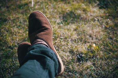 Low section of man wearing shoes while sitting on grassy field