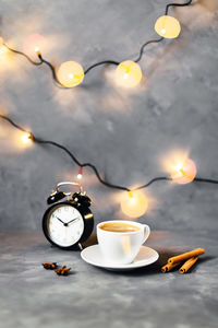 Christmas composition with cup of coffee surrounded by cinnamon, lights and cloves on gray table.
