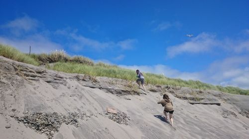 Women climbing hill against cloudy sky