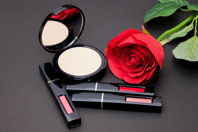 High angle view of red rose by beauty products on table