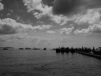 Boats in calm sea against cloudy sky