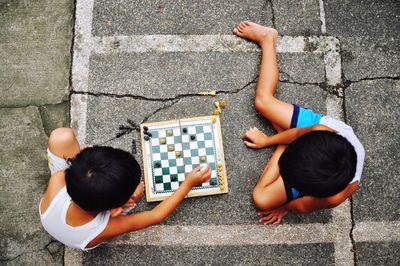 High angle view of friends playing chess while sitting on footpath