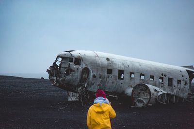 Rear view of woman standing against damaged airplane at beach