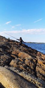 Man on rock by sea against sky