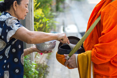 An old asian woman is offering food to buddhist monks at in front home in the morning