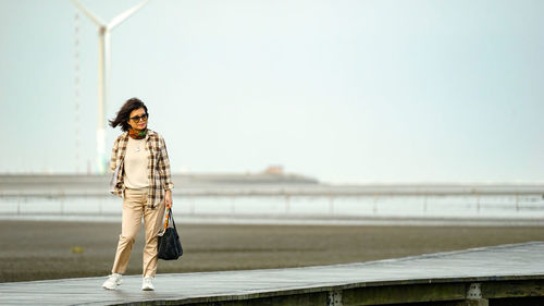 Portrait of young woman standing against railing against sky