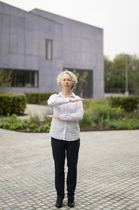 Full length portrait of woman gesturing while standing on footpath against buildings