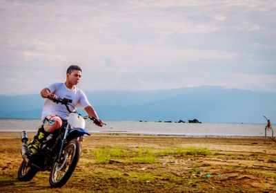Man riding bicycle on sea shore against sky