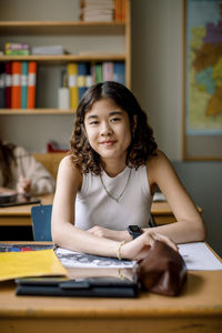 Portrait of girl sitting at desk with book in classroom