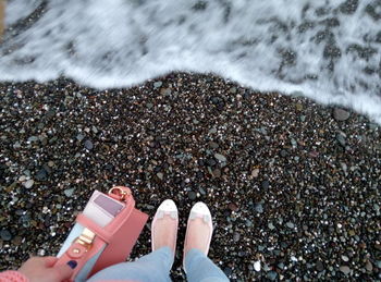 Low section of woman holding bag while standing on shore