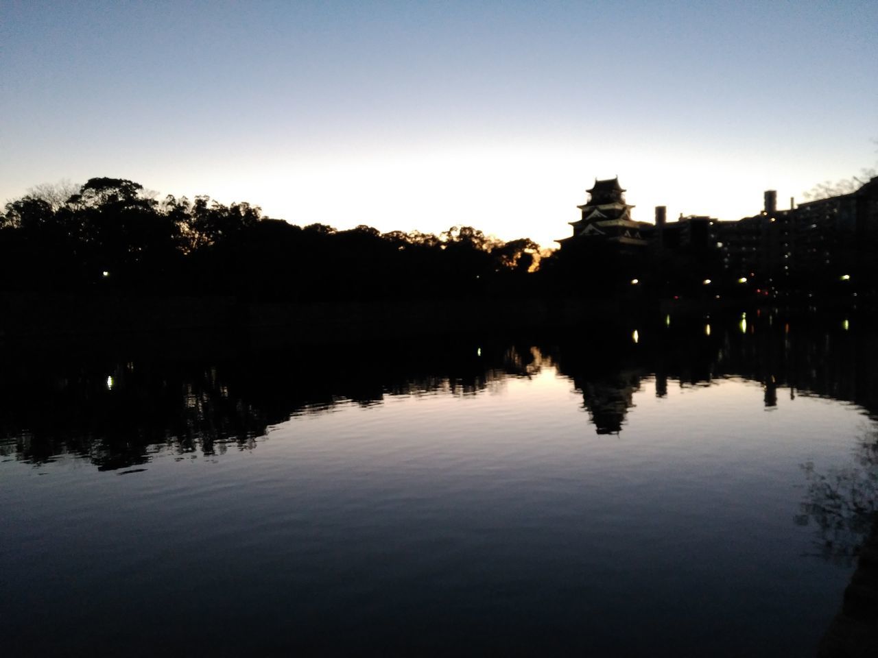 REFLECTION OF SILHOUETTE TREES IN LAKE AGAINST CLEAR SKY AT SUNSET