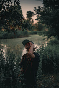 Man standing amidst plants against lake during sunset