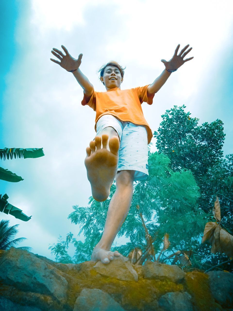 LOW ANGLE VIEW OF WOMAN WITH ARMS RAISED AGAINST WATER