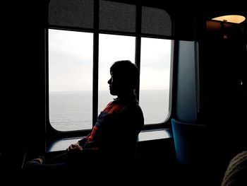 Side view of man sitting by window in ship