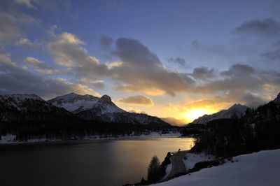 Scenic view of lake by snowcapped mountains against sky during sunset