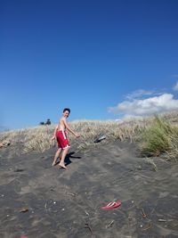 Low angle view of shirtless boy walking on sandy hill against blue sky