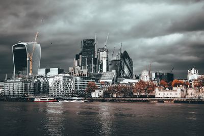 Modern buildings by river against sky in city