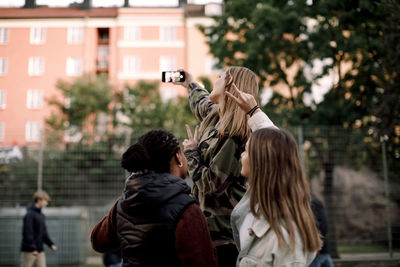 Teenage girls showing peace sign while taking selfie through mobile phone in city