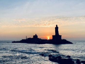 Silhouette of building by sea against sky during sunset