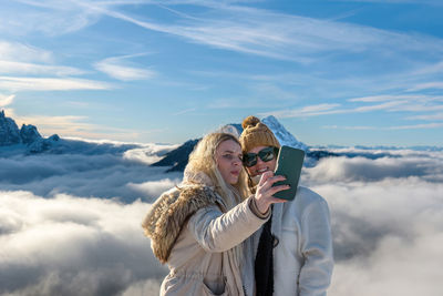 Two female friends taking a selfie in amazing mountains on a sunny day in winter