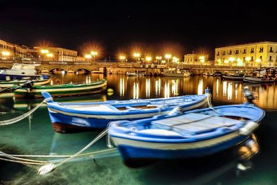 Boats moored at illuminated harbor against sky at night
